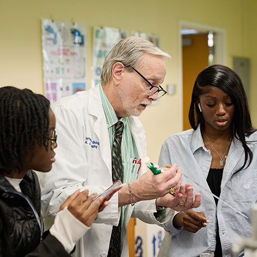 A professor in a lab with two students.